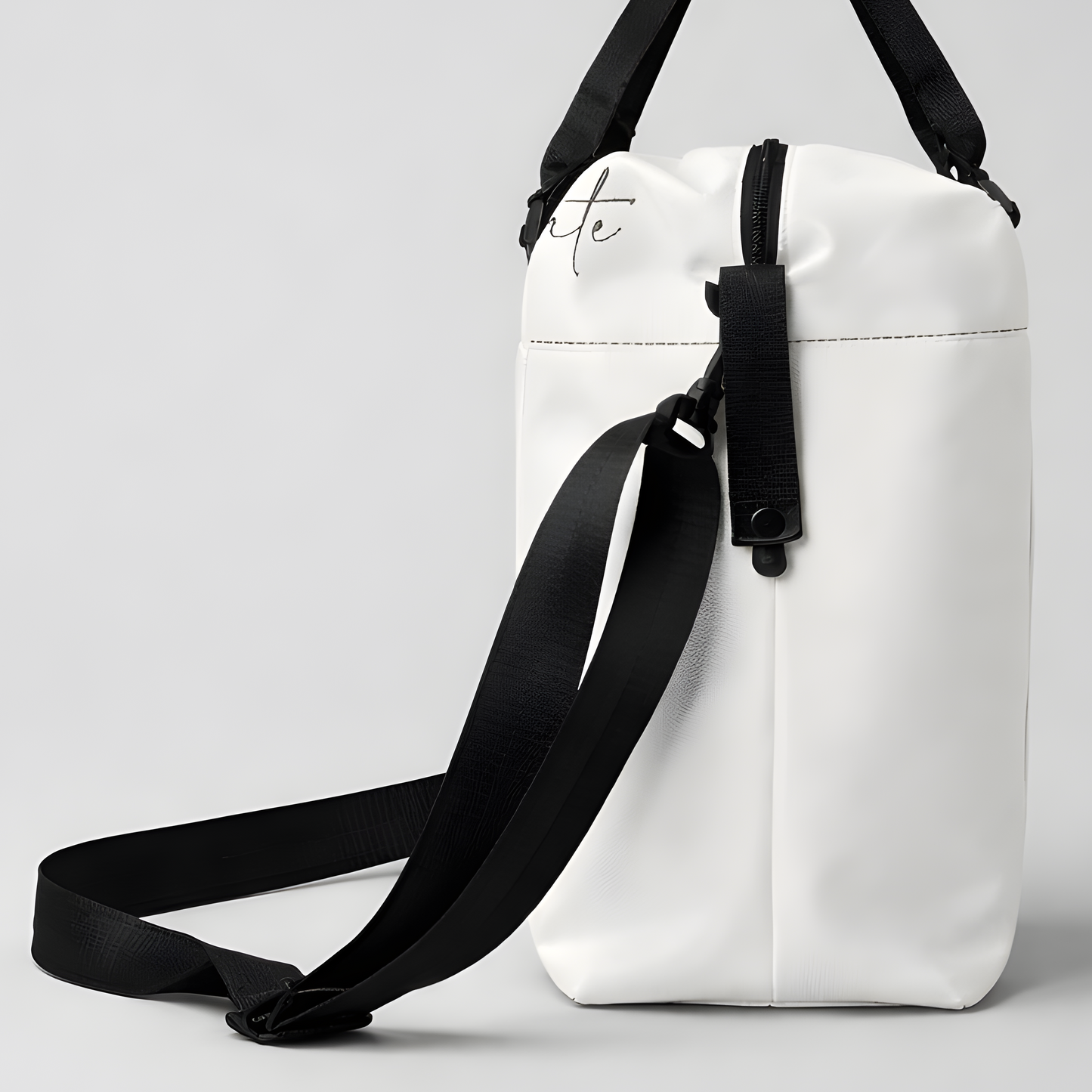White minimalist duffel bag with black straps and subtle cursive logo designed for intentional travel and use