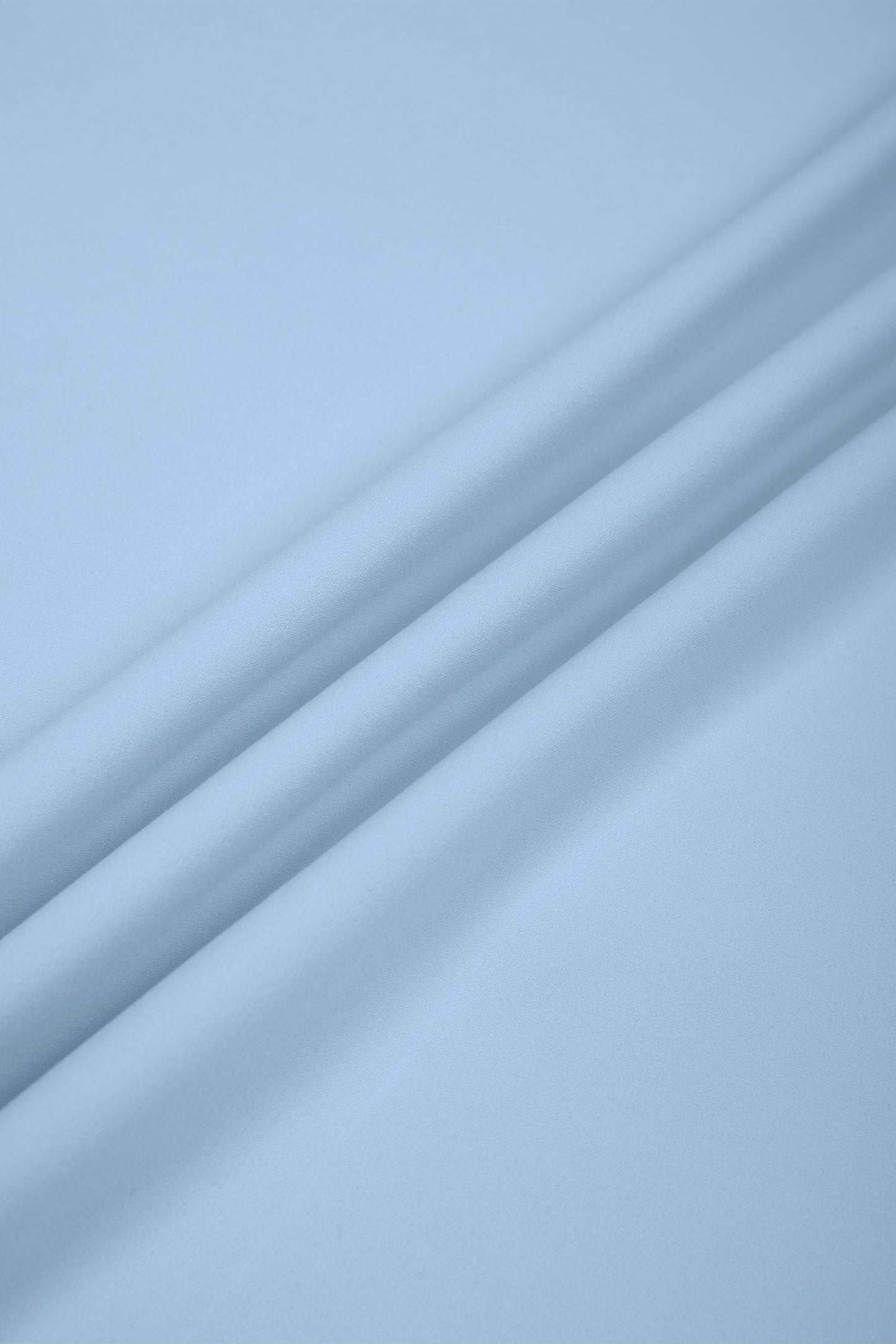 A close-up of light blue fabric with soft diagonal folds and a smooth texture.