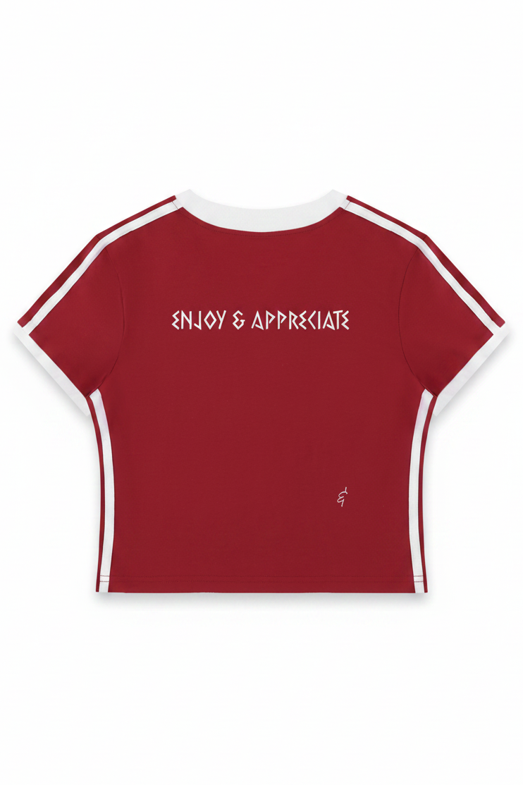 A short-sleeve crop top in deep red with white contrast trim along the collar, sleeve edges, and side panels, featuring the text 'ENJOY & APPRECIATE' printed in white across the chest.