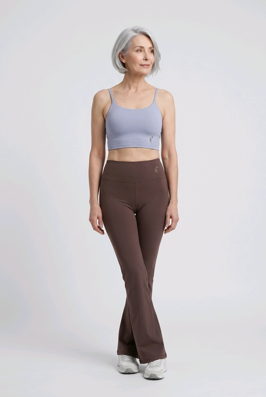 Woman wearing a light blue sports bra and brown flared pants on a white background