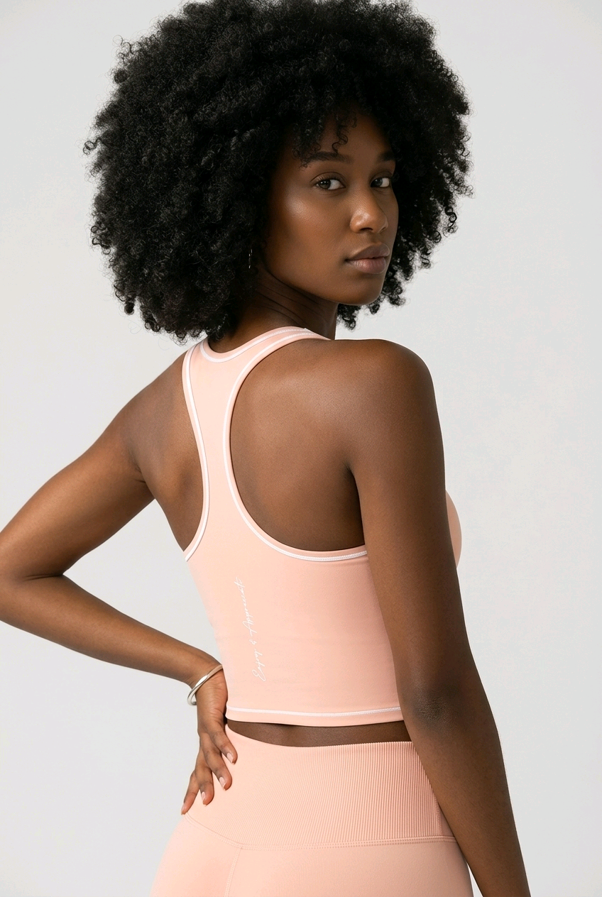 A woman with a large black afro is shown from the back wearing a light peach-pink athletic crop top and matching leggings against a light gray studio background.