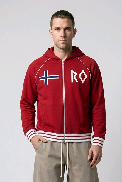 A man modeling a red zip-up hoodie with a white front zipper, white drawstrings, a white and blue Nordic flag on the left chest, and 'RO' in white on the right chest. He is wearing beige drawstring sweatpants and white sneakers against a light gray studio background.