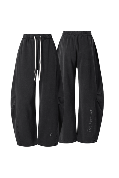 A pair of black wide-leg sweatpants shown from the front and back against a plain white background. The front view shows a white drawstring, and the back view shows a small white script logo near the lower left leg.
