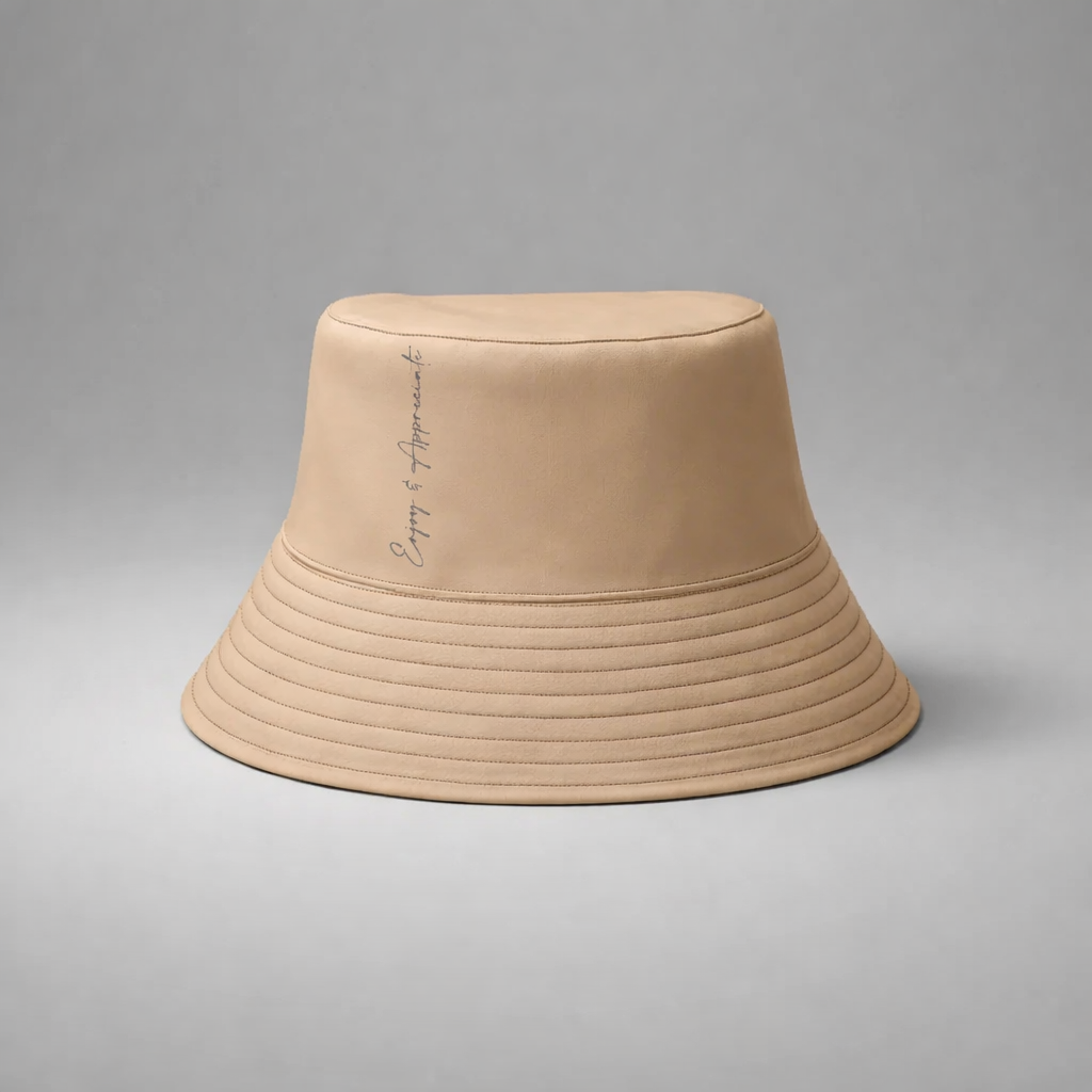 Beige bucket hat with subtle vertical stitching and delicate enjoy and appreciate script embroidery on the side