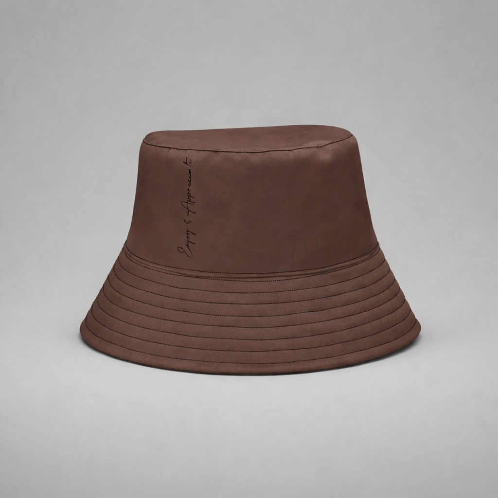 A brown bucket hat with subtle stitched texture and embroidered phrase on the side