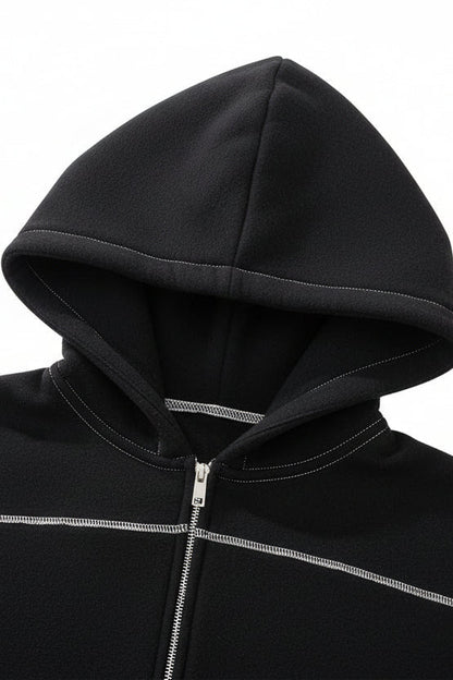 Close-up of a black zip-up hoodie with a hood, featuring contrasting light gray stitching and a silver zipper.