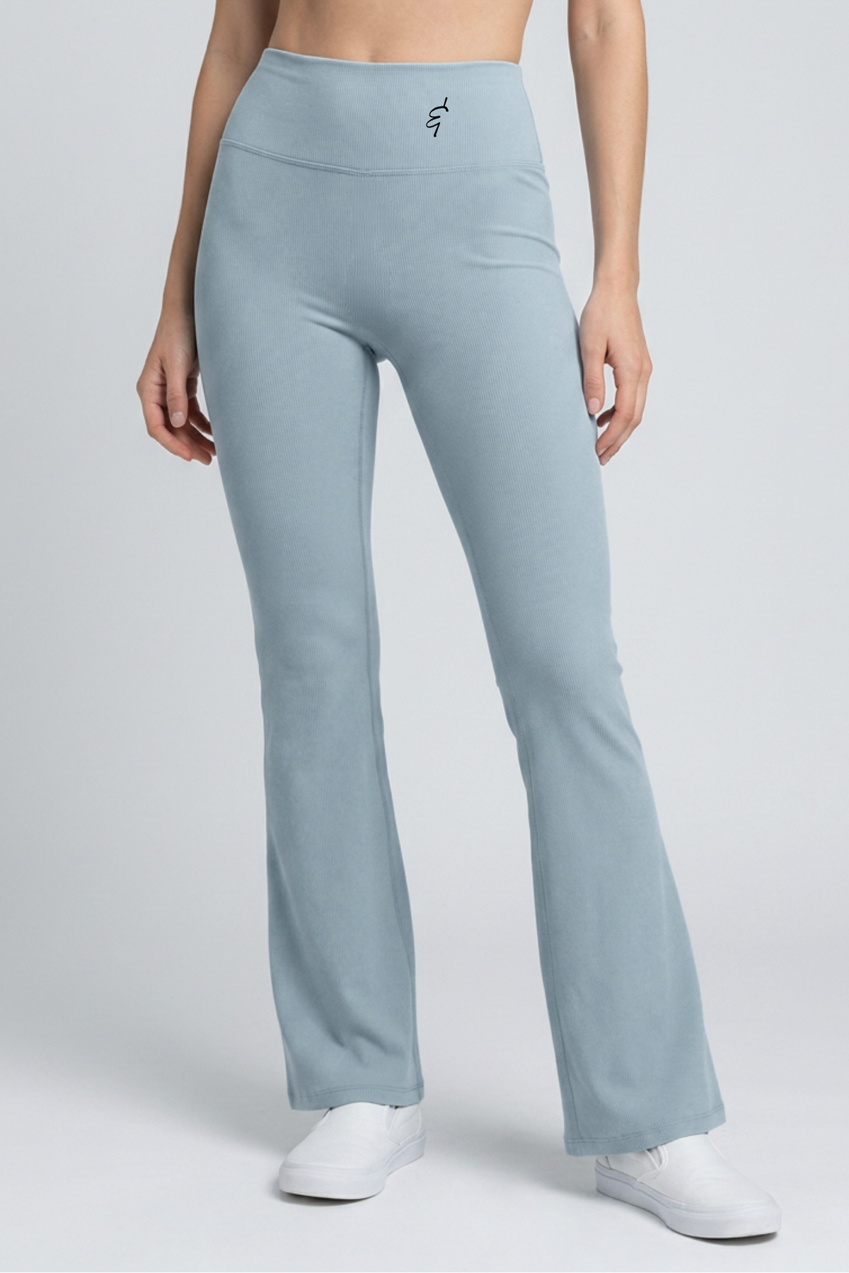 A model wearing light blue high-waisted flared leggings and a matching cropped top, paired with white sneakers, against a light gray studio background.