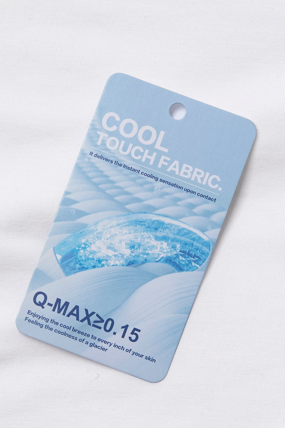 A light blue fabric care tag labeled 'COOL TOUCH FABRIC' and 'Q-MAX>=0.15' with a water ripple graphic, placed on a white textured fabric background.
