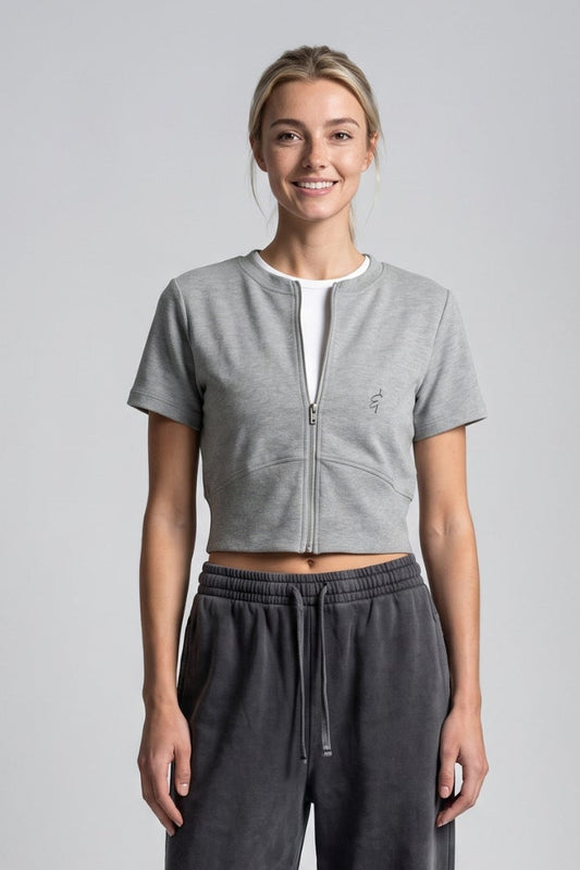 A woman modeling a light gray short-sleeve cropped top with a split V-neck and dark gray wide-leg drawstring sweatpants against a light gray studio background.