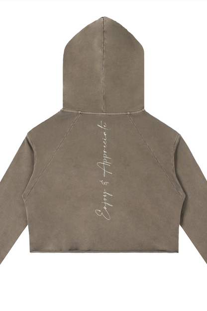 A cropped coffee colour raw edge hoodie with subtle enjoy and appreciate embroidery on the back