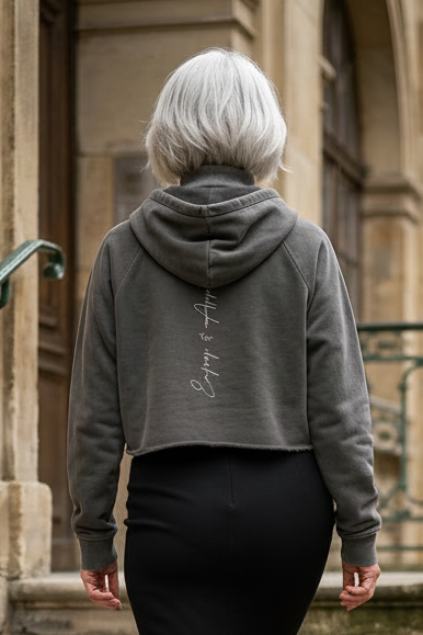 A dark gray cropped raw edge hoodie with a subtle cursive script design on the back side