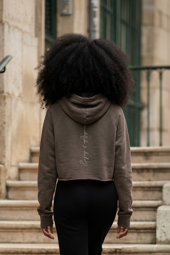 A taupe cropped raw edge hoodie showing the back with subtle embroidered script on soft fabric