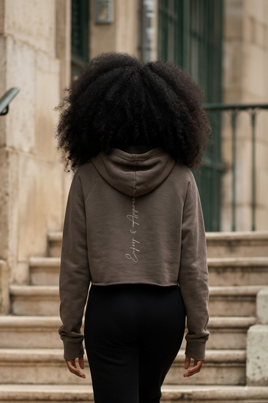 A taupe cropped raw edge hoodie showing the back with subtle embroidered script on soft fabric