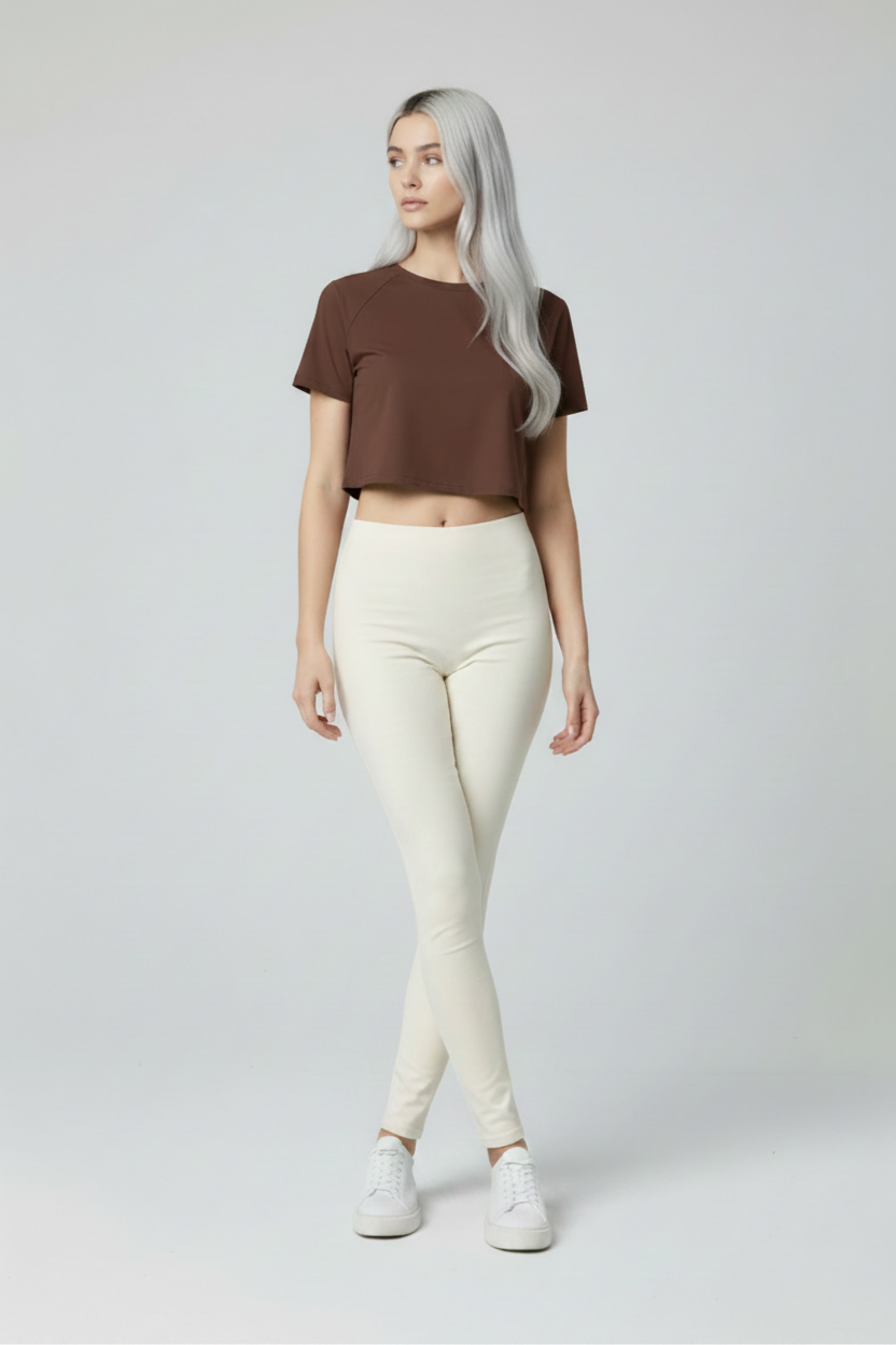 Woman wearing a brown crop top and cream pants on a plain background