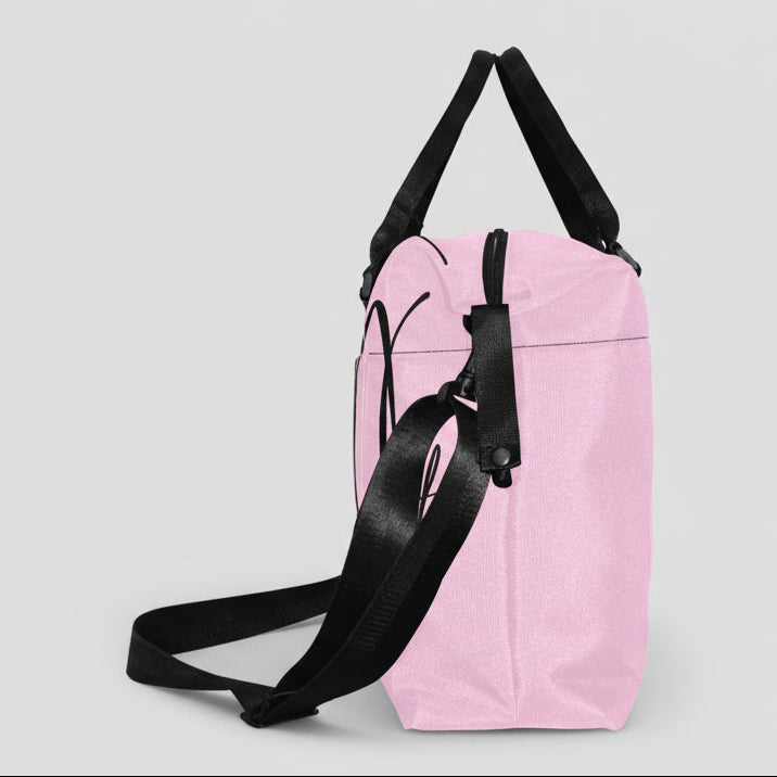Pink canvas duffel bag with black handles and detachable shoulder strap featuring bold black cursive lettering