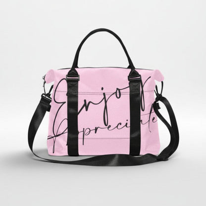 Pink duffel bag with black handles and shoulder strap featuring enjoy appreciate in elegant cursive script