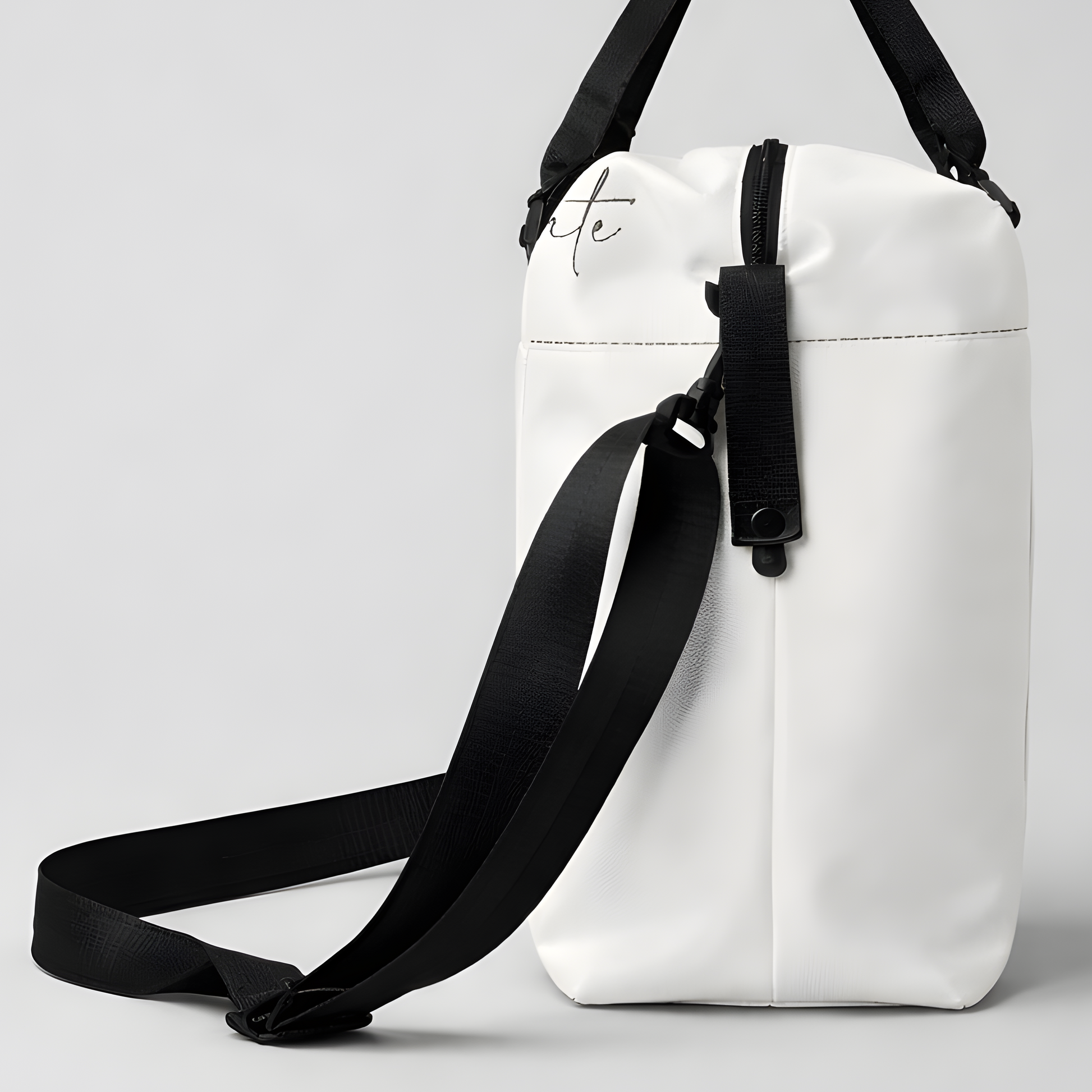 White minimalist duffel bag with black straps and subtle cursive logo designed for intentional travel and use