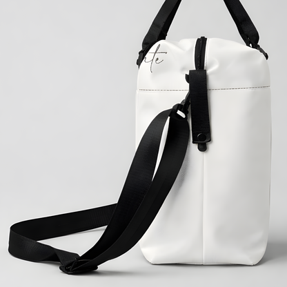 White minimalist duffel bag with black straps and subtle cursive logo designed for intentional travel and use