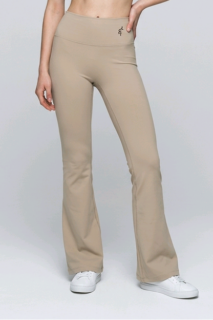 A woman wearing beige high-waisted seamless flared leggings paired with a brown sports bra and white sneakers