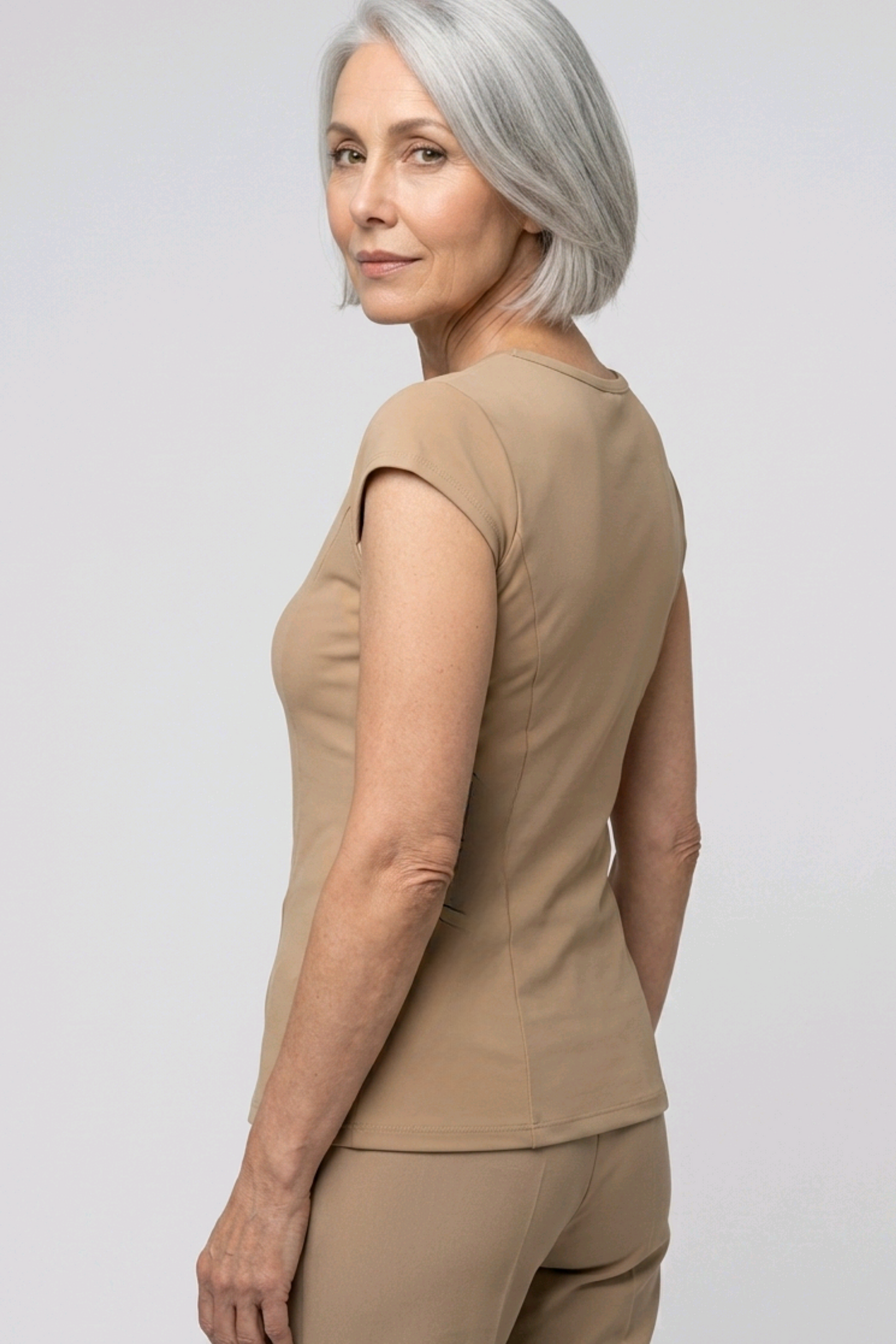 Woman wearing a camel colour top and pants on a light gray background