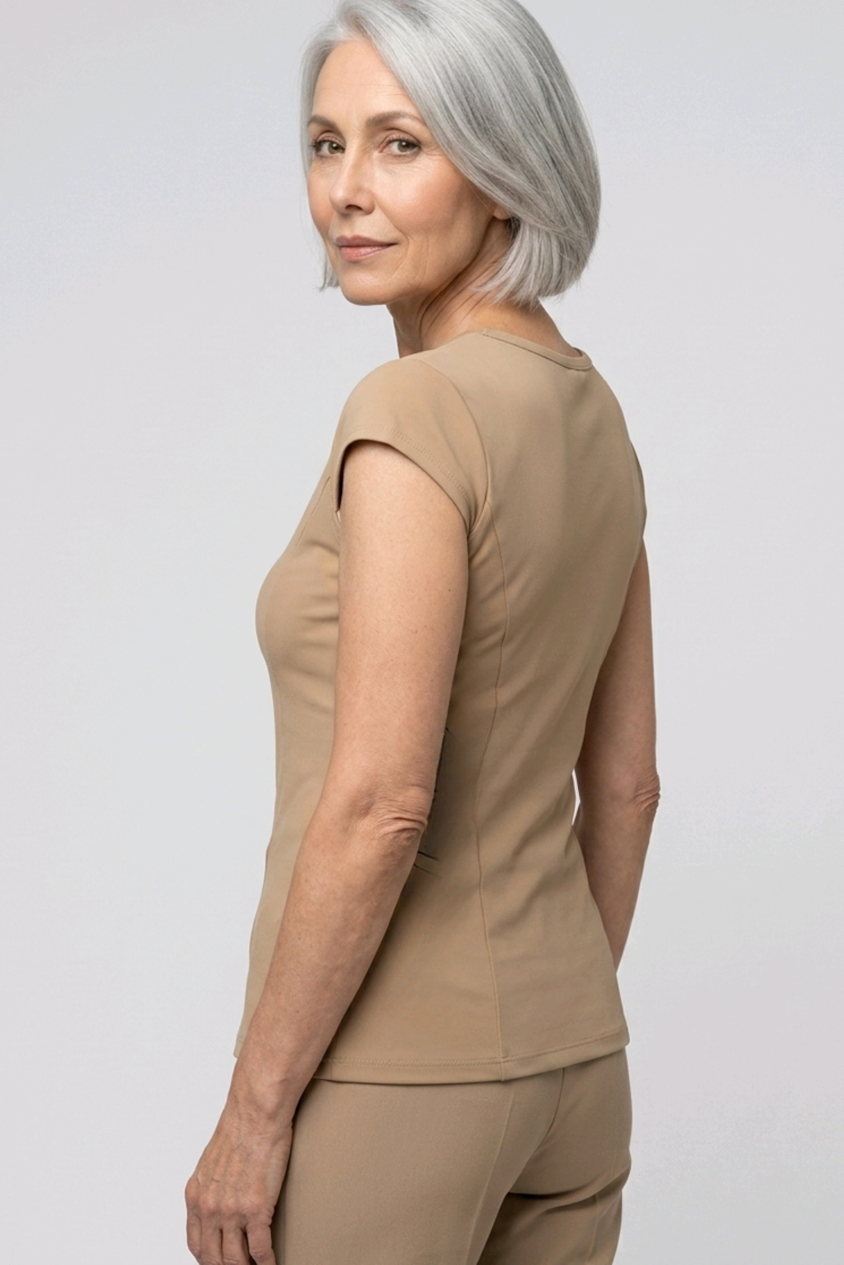 Woman wearing a camel colour top and pants on a light gray background