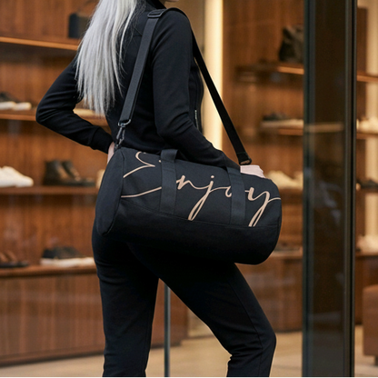Black gym duffel bag with gold cursive enjoy lettering and adjustable shoulder strap for easy carrying