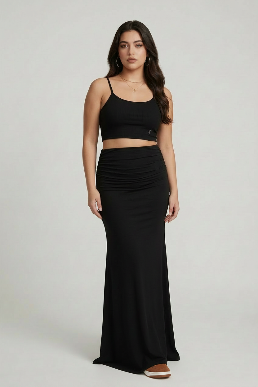Woman wearing a black crop top and long black skirt wearing brown and white shoes on a light gray background
