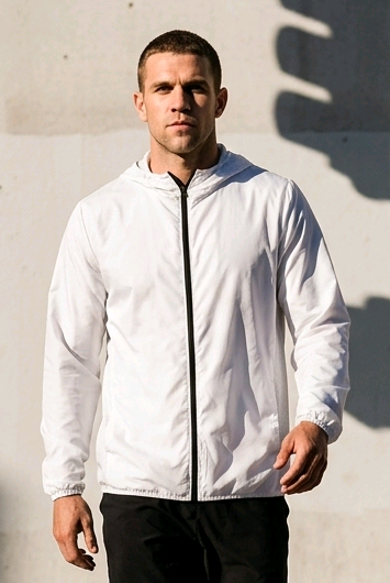 Man in white jacket and black shorts walking on a city street with traffic lights and shadows on the wall.