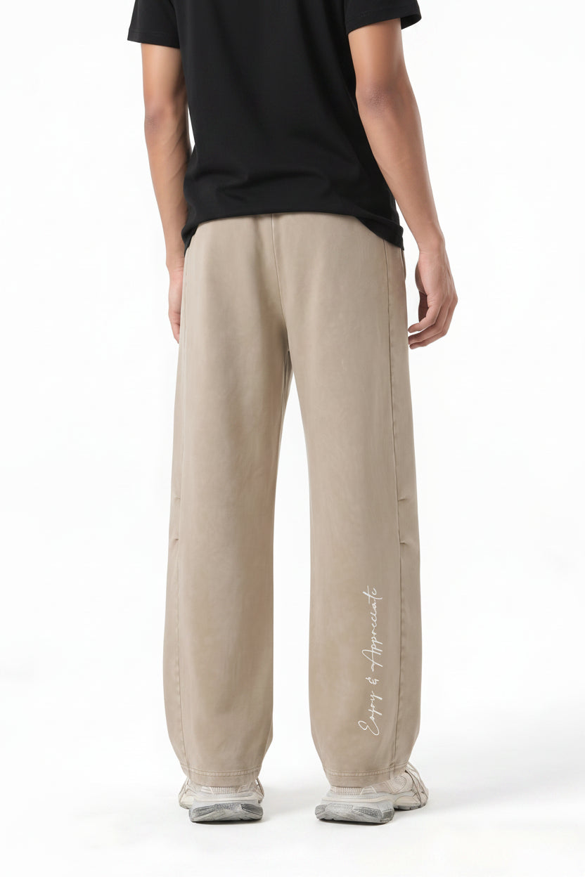 A model shown from the back wearing beige wide-leg sweatpants with a white script logo on the lower left leg, photographed against a clean white background.
