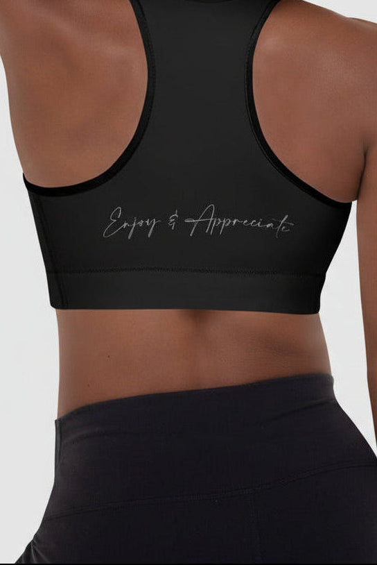Back view of a black racerback sports bra with silver enjoy and appreciate embroidery on the back
