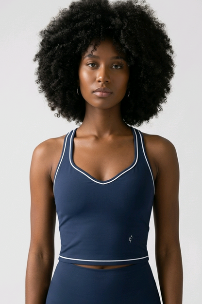 A woman with a large black afro wearing a navy blue athletic tank top with white piping and matching navy bottoms, photographed against a light gray studio background.