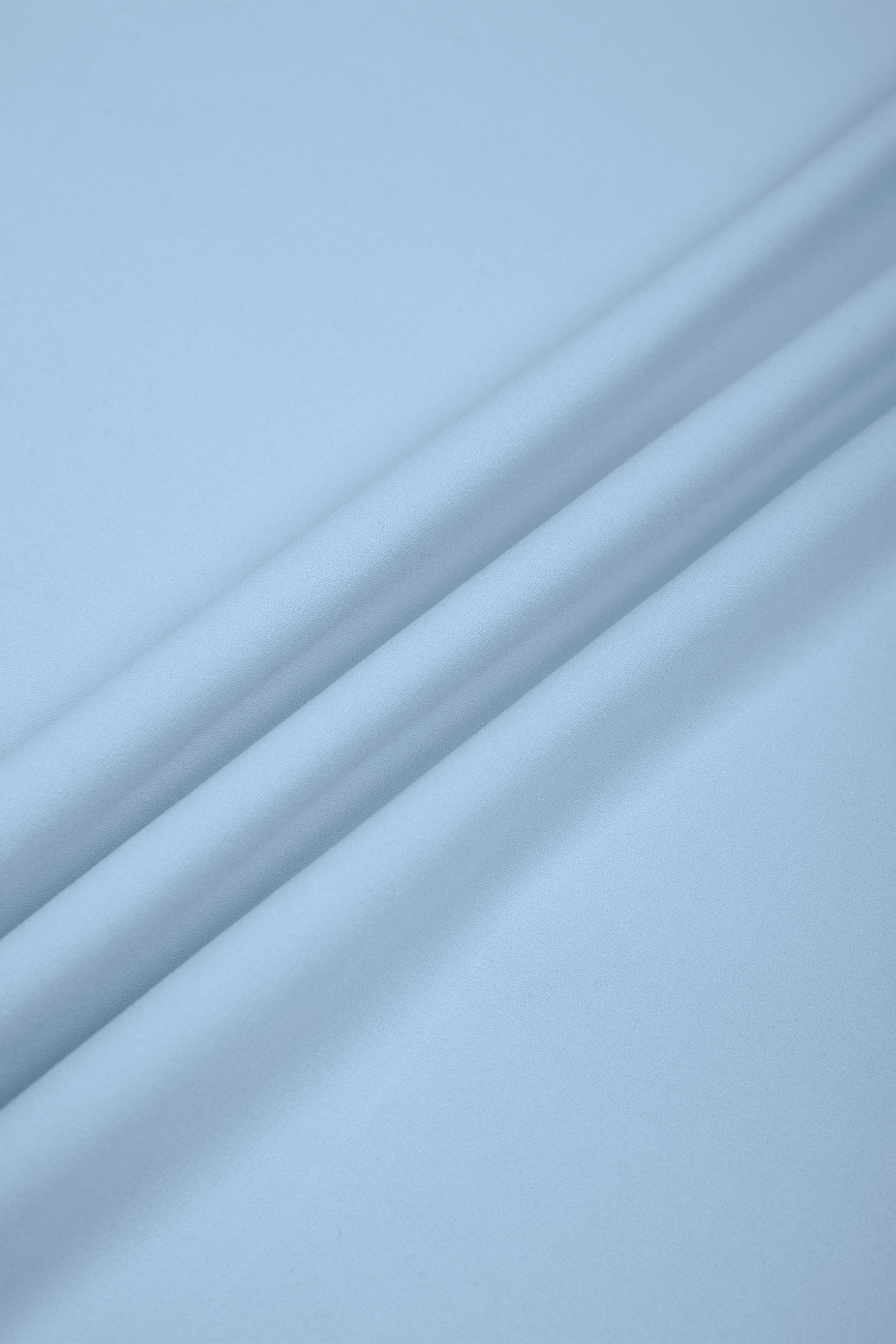 A close-up of light blue fabric with soft diagonal folds and a smooth texture.