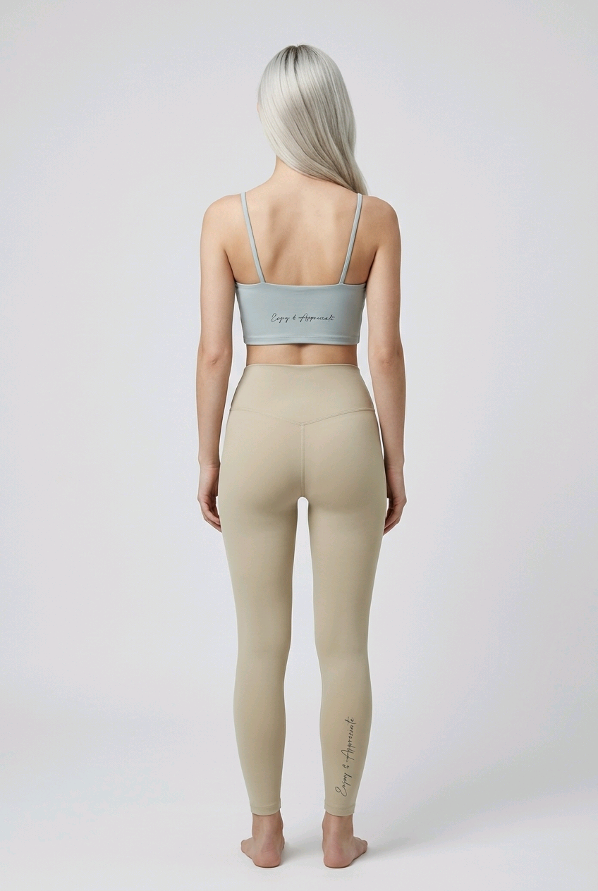 A light gray seamless sports bra with spaghetti straps and a subtle cursive inscription on the back side