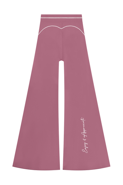 A pair of dusty rose wide-leg pants with white contrast stitching, featuring a curved white line detail near the waistband and white script text on the lower left leg, displayed on a solid white background.