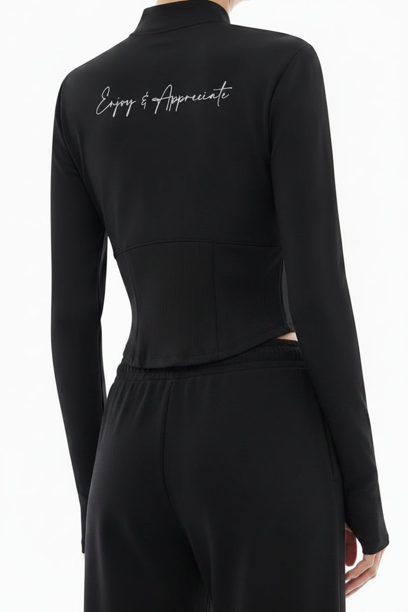 A model shown from the back wearing a black mock-neck long-sleeve top with white script embroidery on the upper back and light gray wide-leg sweatpants, set against a plain white background.