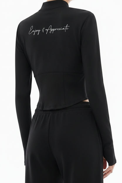 A model shown from the back wearing a black mock-neck long-sleeve top with white script embroidery on the upper back and light gray wide-leg sweatpants, set against a plain white background.