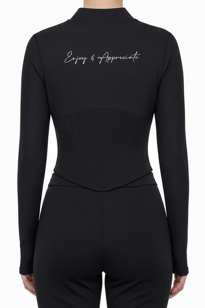 A model shown from the back wearing a black mock-neck long-sleeve top with white script text on the upper back and light gray wide-leg sweatpants, against a plain white background.