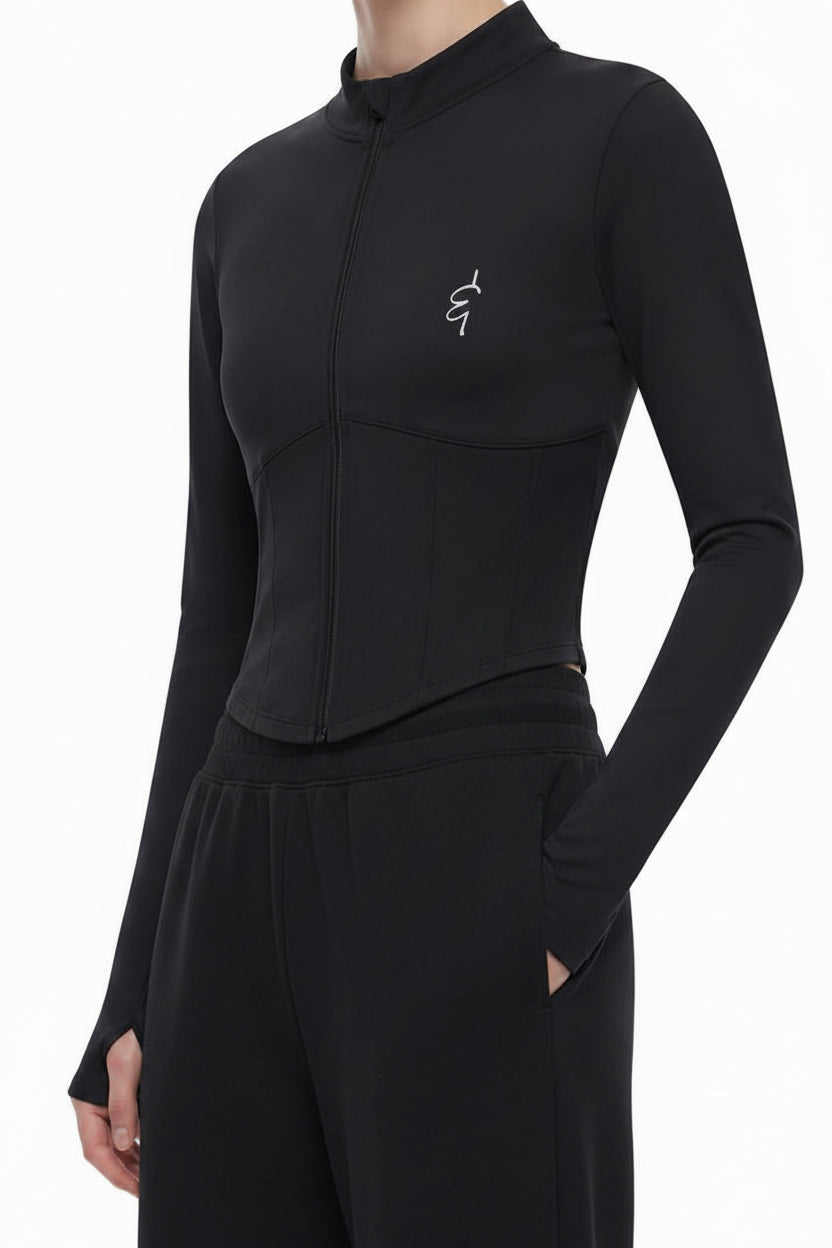 A woman modeling a black mock-neck long-sleeve top with a small embroidered logo on the chest, paired with light gray wide-leg sweatpants, against a plain white studio background.
