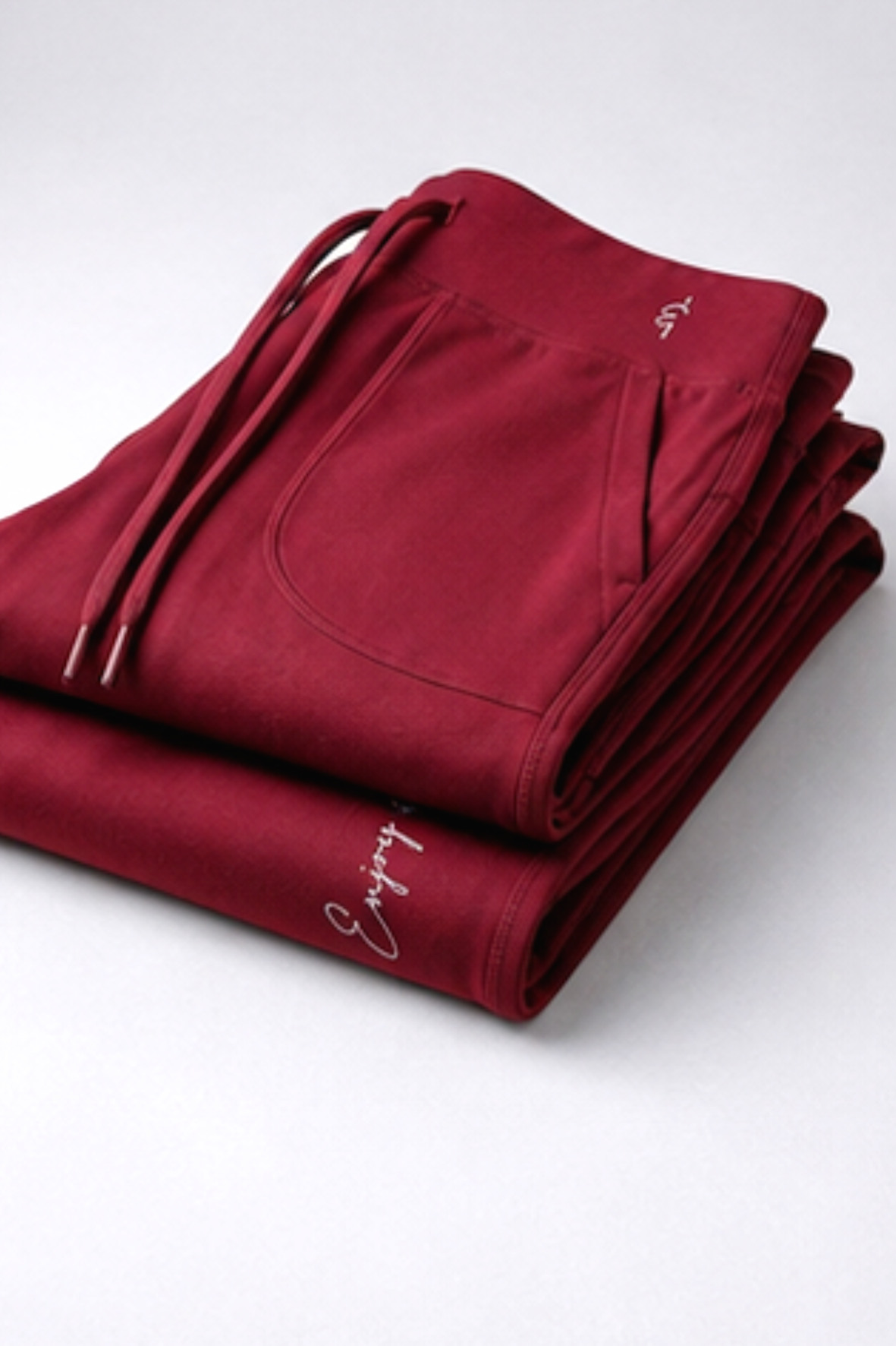 A folded pair of deep burgundy drawstring sweatpants with a small white script logo on the side, displayed on a clean white background.