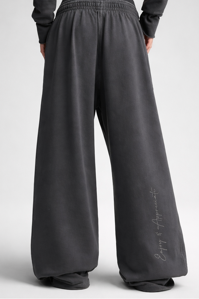 Dark gray wide leg sweatpants with elastic waistband and cursive script detail on the side made of soft material
