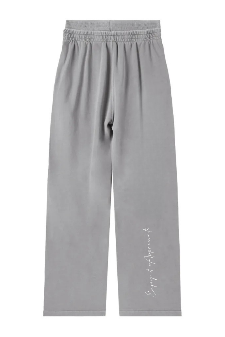 Gray wide leg sweatpants with a relaxed fit elastic waistband and white cursive enjoy & appreciate script on the lower leg