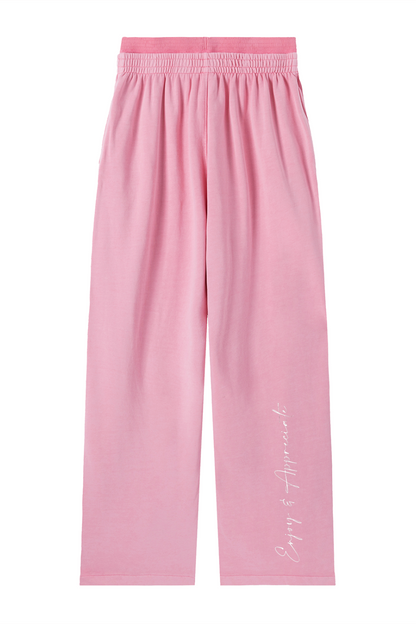 Pink wide-leg lounge pants with an elastic waistband and a white cursive 'Enjoy & Appreciate' logo printed down the left leg, shown flat on a white background.