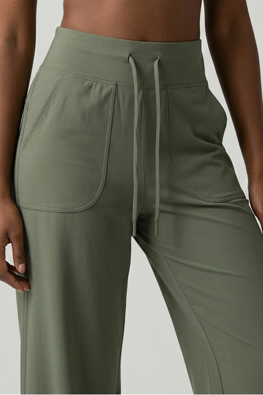A model wearing a black sports bra and olive green drawstring pants against a light gray studio background.