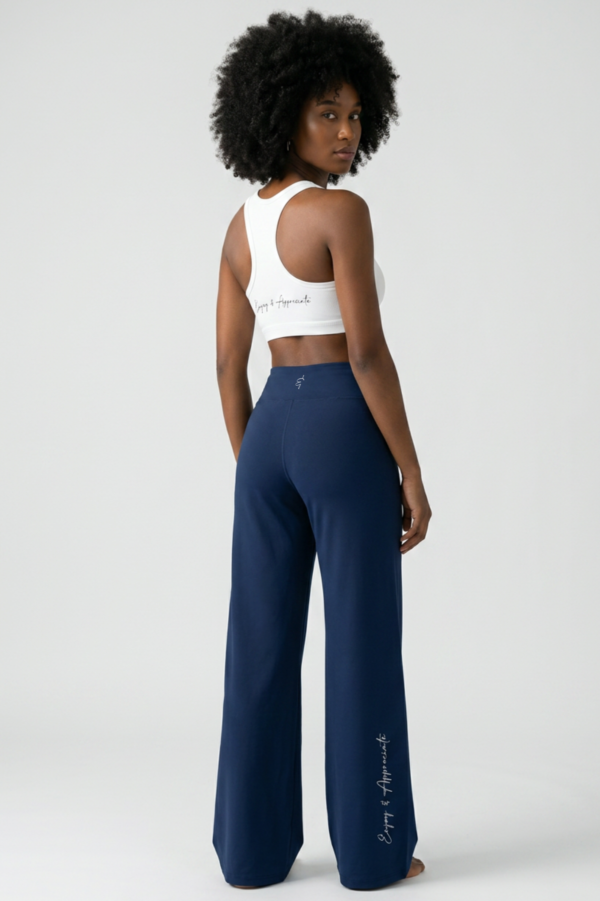 Woman wearing High Rise Pocket Pants in navy blue with a white sports bra, back view, light gray studio background, by Lilliroa