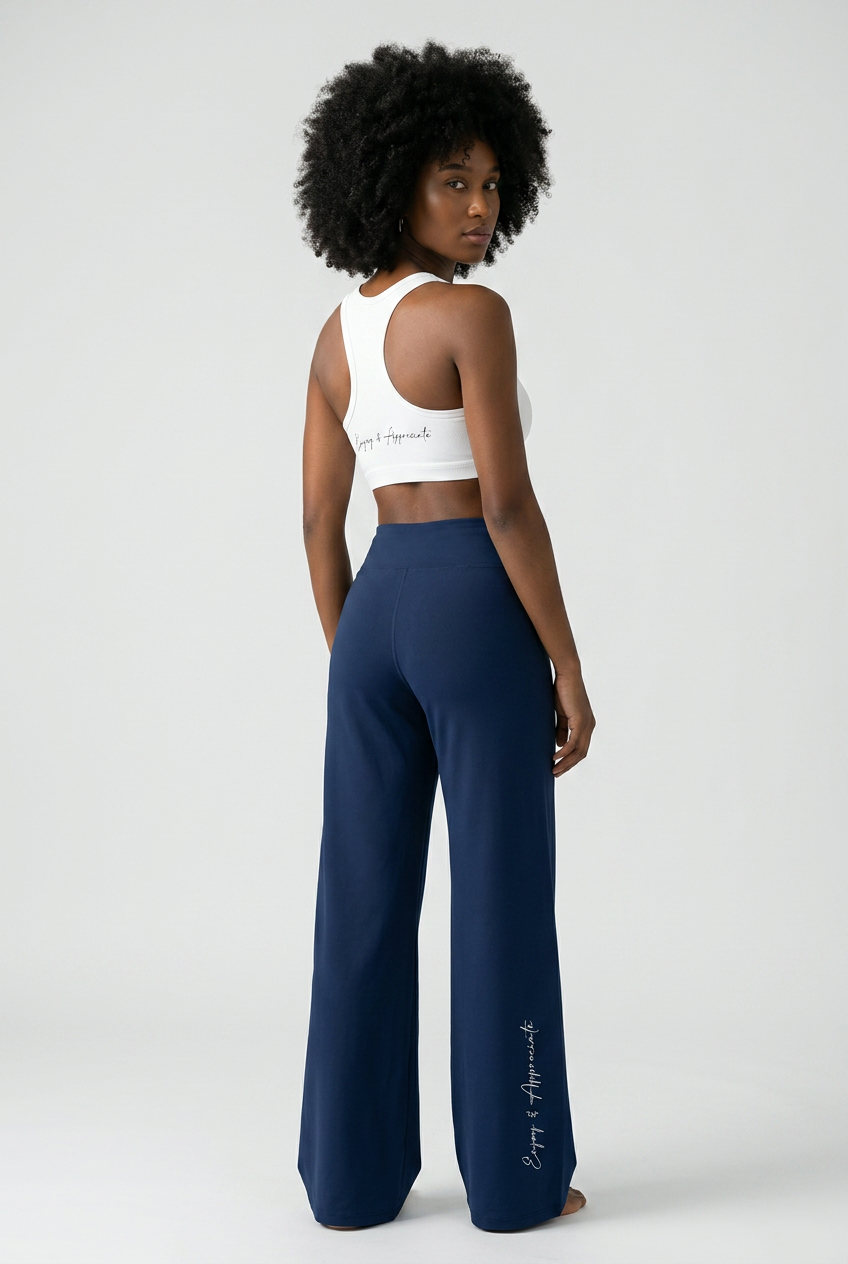 A model shown from the back wearing navy blue wide-leg pants and a white sports bra, photographed against a light gray studio background.