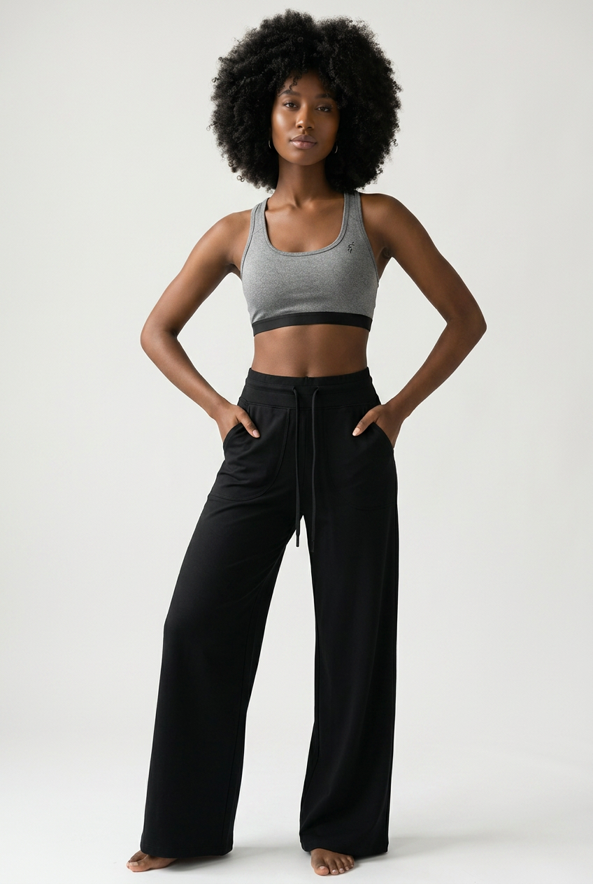 A woman modeling a gray sports bra and black wide-leg pants against a light gray studio background.