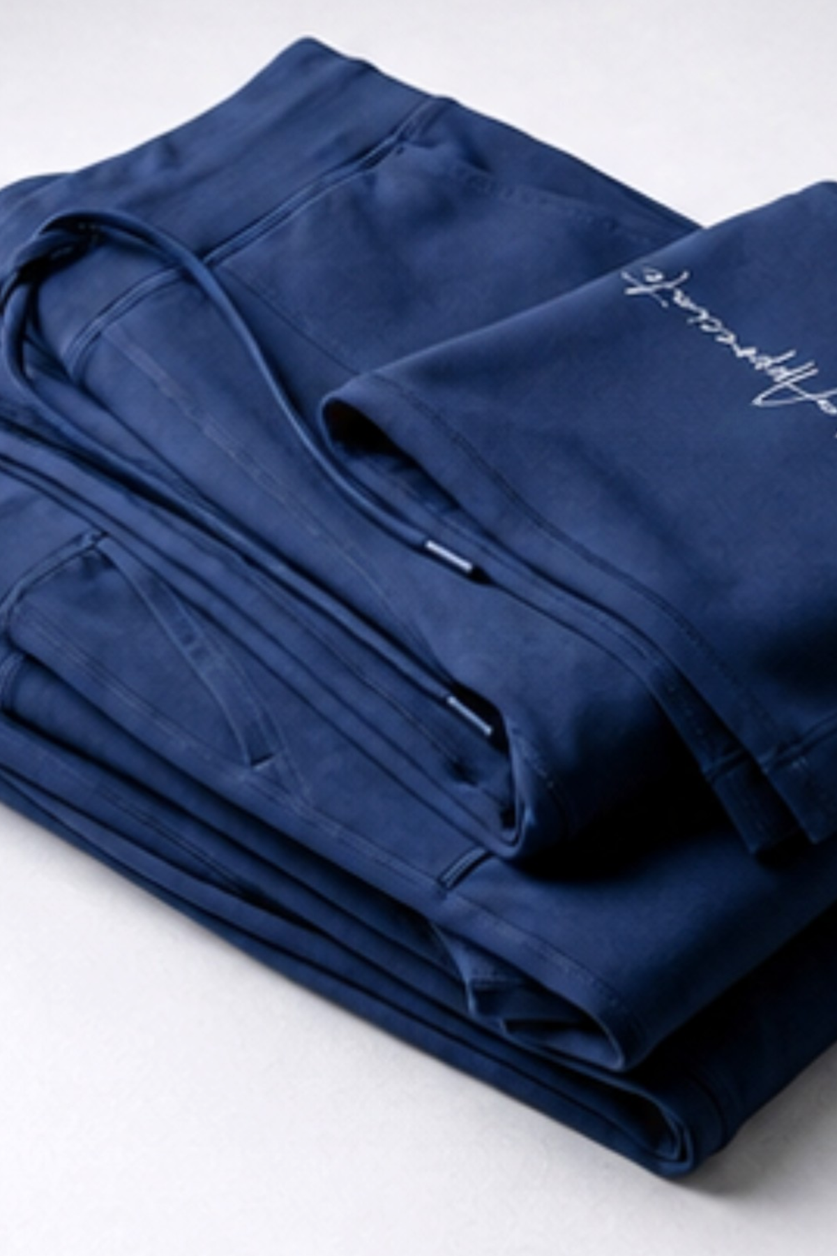 A folded pair of navy blue scrub pants with white embroidered script on the leg, displayed on a light gray background.