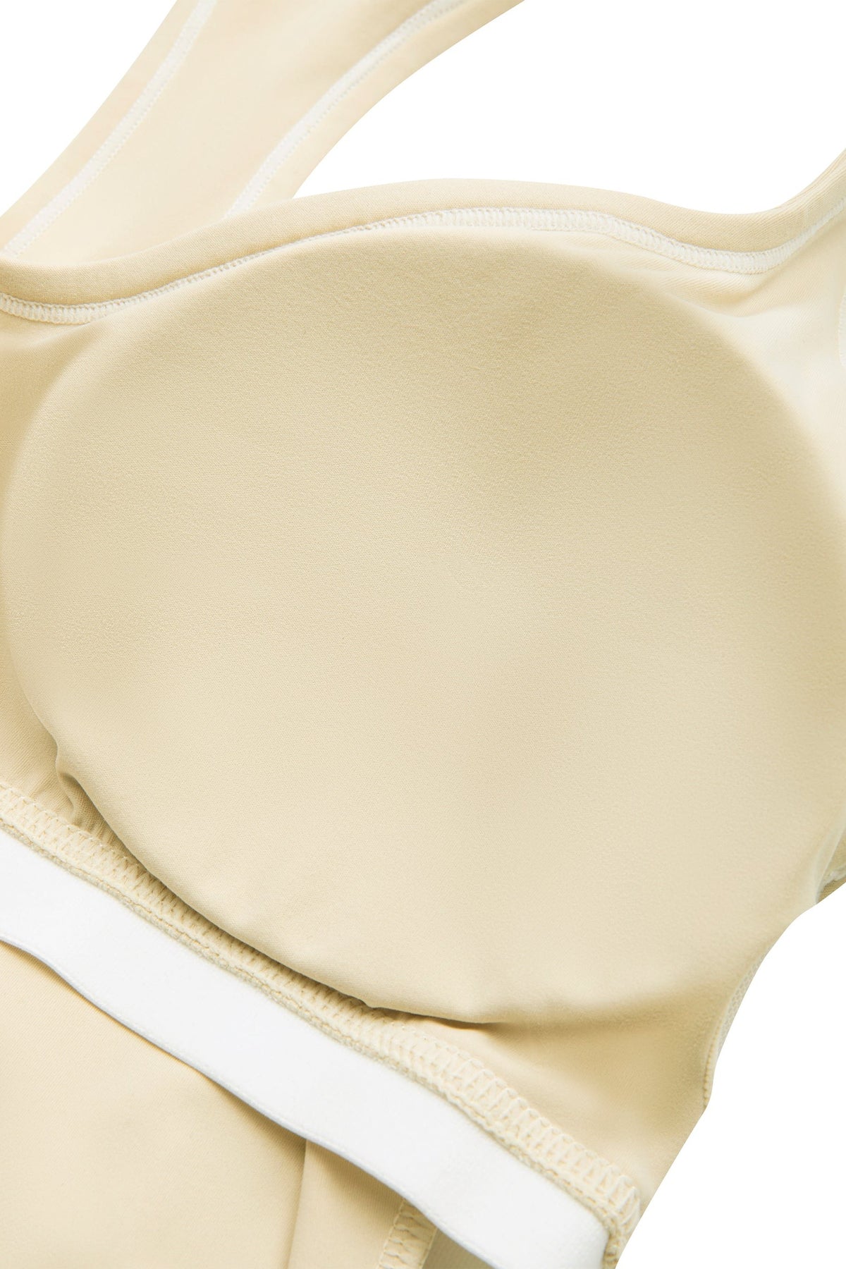 Close-up of a beige sports bra with a smooth, molded underwire cup and white trim along the neckline and band.