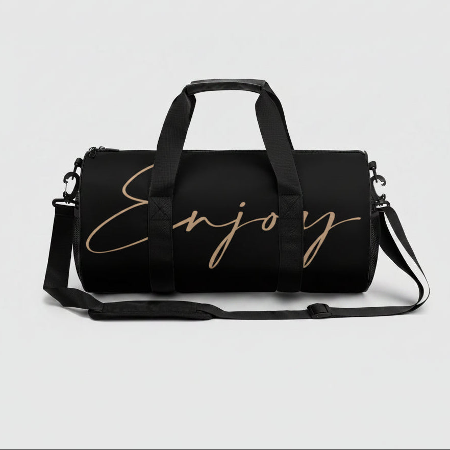 Black gym duffel bag with gold cursive enjoy lettering and adjustable shoulder strap for easy carrying