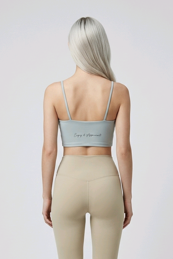 Light gray sports bra with thin straps and subtle cursive inscription on back paired with high waisted seamless leggings